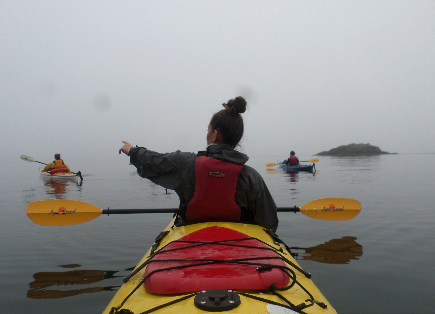 View of a young woman in a kayak from behind, pointing in the distance 